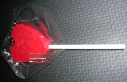 A small, heart-shaped lollipop in its wrapper.