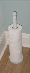 Vertical toilet roll holder of wood with a paint finish, holding three individual rolls of toilet paper.  There is room for a fourth.