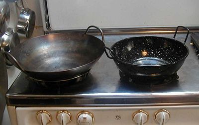 A wok sits next to a karahi on a Western-style stove. Note that the flat-bottomed karahi (right) is sitting on an ordinary burner cover, while the round-bottomed wok is balanced in a wok-ring.